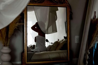 Moody mirror reflection of Emily Michele wrapped in white fabric, sitting gracefully in a softly lit bedroom — representing intimacy, reflection, and self-awareness through the Unveiled journey.