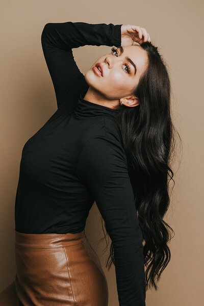 Denver boudoir photographer posing for a headshot in her boudoir studio wearing a black turtleneck and leather skirt