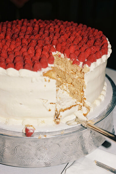 A cut wedding cake with raspberries on top 