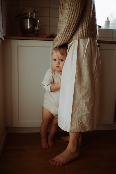 ett barn håller om sin mammas ben hemma i köket