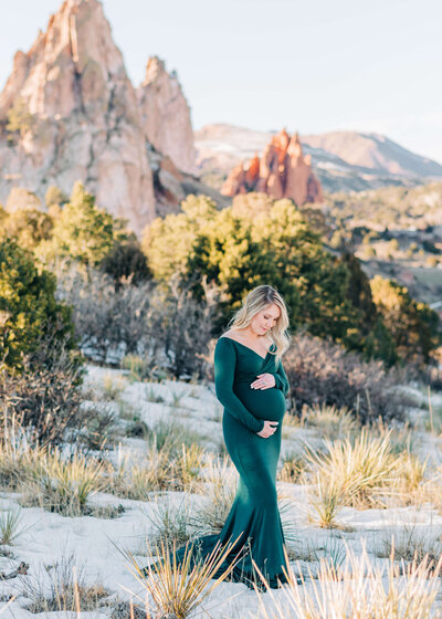 pregnant woman standing at garden of the gods during winter hugging belly