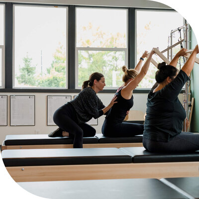 Teacher helping women practice push through on Pilates tower during a semi-private session