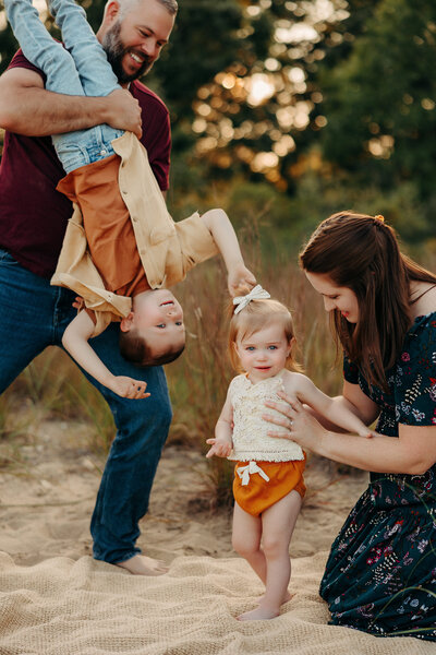 Father playfully holding his child upside down while the pregnant mother laughs.