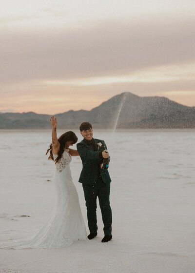Couple popping champagne after eloping at the Bonneville salt flats in Utah