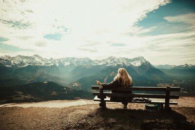 woman sitting on a bench looking at mountains