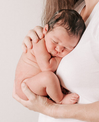 naked newborn baby sleeping in mother's arms photo taken by rosa ashdown
