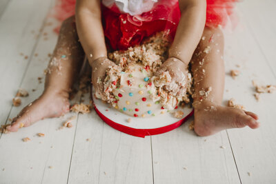 little girl sitting on floor smashing birthday cake