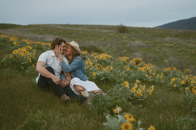 a couple sitting in the wildflowers at dusk leans in for a kiss
