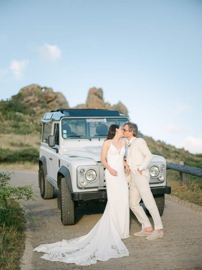 Stylish couple sharing a kiss beside a Land Rover under soft evening light in St Barth — Destination Wedding Photographer Portfolio.