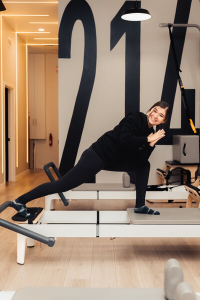 Headshot of Pilates instructor  standing in front of Pilates214 neon logo sign.