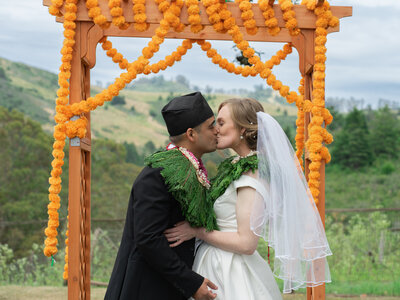Enchanting photograph capturing a bride and groom sharing a heartfelt kiss under the wedding altar, set against the scenic beauty of Half Moon Bay.