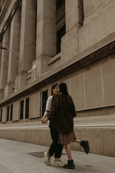 couple holding hands and kissing in front of building