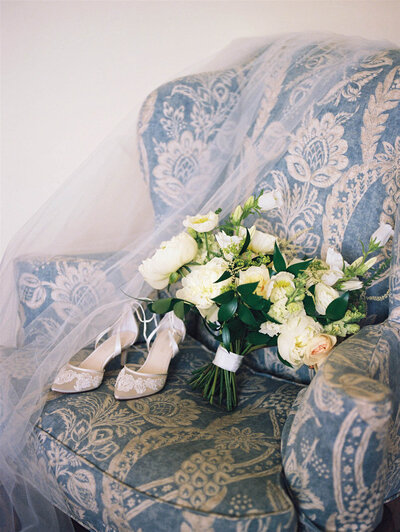Shoes and bouquet on a vintage patterned chair with veil draped over it.