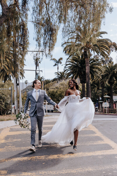 Destination wedding photographer captures Catalina Island elopement couple holding hands and running across the street