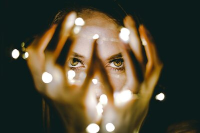 A close-up of a woman's eyes, framed by her hands holding glowing lights, creating a captivating and mysterious effect. This image is for Debra LeClair's Embodied Style services.