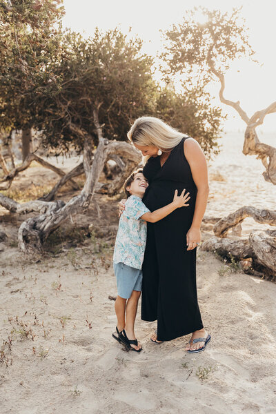 a pregnant woman hugs her young son during their maternity photography session at mission beach in san diego