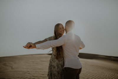 Husband and wife dancing in the sun's glow at the sand dunes, celebrating their first wedding anniversary.