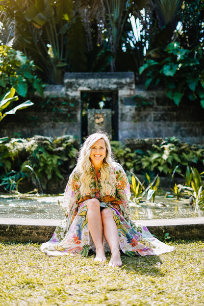 Katie, spiritual entrepreneur coach, sitting in a bright-colored dress, posing for a photo in the warm glow of sunlight, radiating positivity and energy.