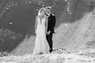 This timeless black and white photograph captures the bride and groom looking at each other atop a mountain during their perfect summer helicopter elopement. The dramatic setting and elegant simplicity of the image highlight the beauty and intimacy of their unforgettable day.
