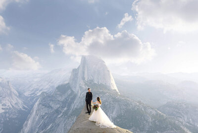 A bride and groom stand in front of Half Dome with a giant blue sky on their Yosemite Elopement.
