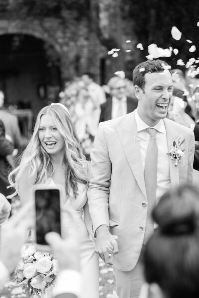 A black and white candid moment of a bride and groom leaving their ceremony with a petal toss by Florida wedding photographer Angelika Krug Photo & Film