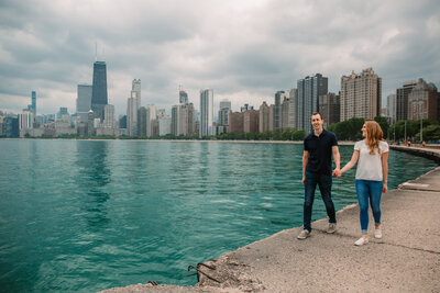 soon to be husband and wife stroll by lake michigan with chicago in the background