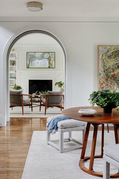 Interior decorators in Boston created a modern look in a historic New England home with a white foyer, arched entry, walnut pedestal table and bench, and modern art.