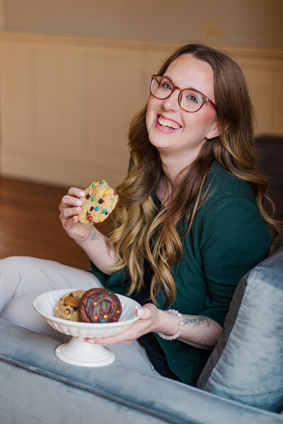 Brand photography with woman sitting on a leather couch wearing a red cardigan and posing for Virginia Beach photographers