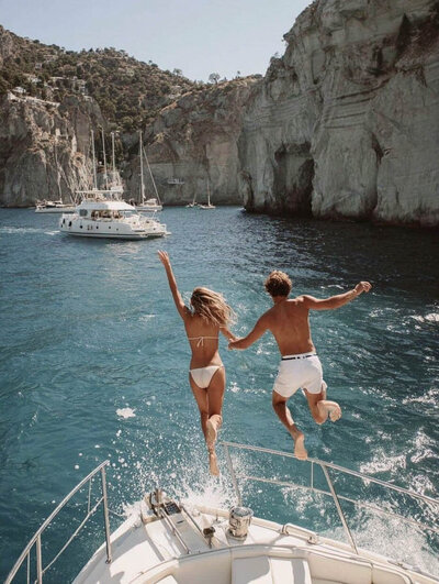 Couple jumping into turquoise Mediterranean waters from sailboat during adventurous travel experience. Tailored Oasis Travel Co.