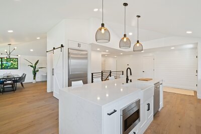 A clean and modern new kitchen renovation completed by United Contractors featuring a white marble countertop, new stainless steel appliances, recessed lighting, and pendant light fixtures hanging above the island.