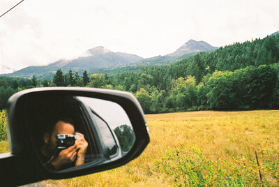 man taking photo through car mirror