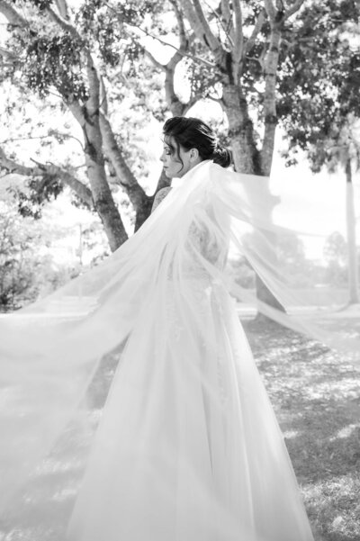 A bride in a white dress stands gracefully on lush green grass, embodying elegance and joy on her special day.