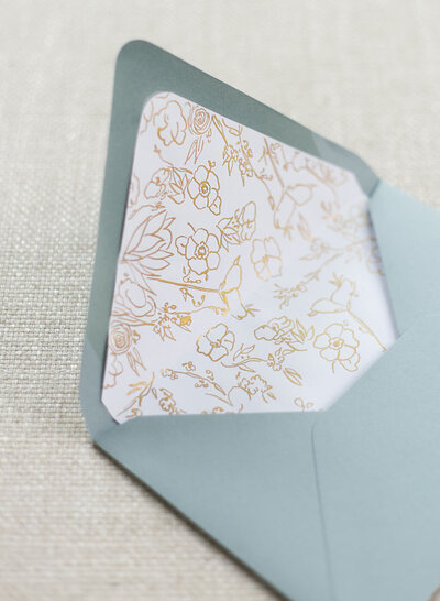 Hand-drawn-gold floral envelope liner inside a dusty blue envelope