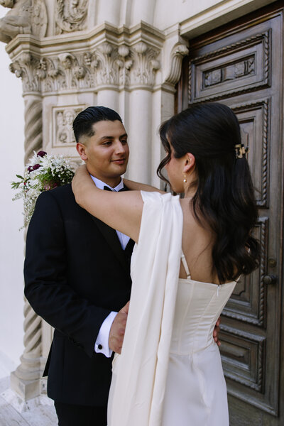 Bride and groom standing in front of a building dancing.
