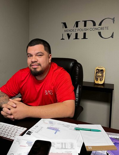 High-quality concrete polishing expert in a professional office setting, dressed in a red branded uniform. The desk is equipped with contracts and important documents, reflecting a high level of expertise and professionalism.