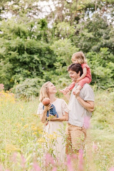 Family stands in filed of flowers during outdoor newborn photo session with Sara Sniderman Photography at Heard Farm in Wayland Massachusetts