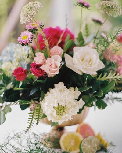 colorful floral arrangement in a brass vase with fruits at the bottom