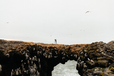 Couple walking together on a rocky coastal shoreline in Iceland — destination wedding photo