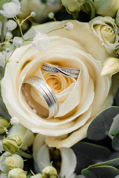 Close-up of two wedding rings nestled inside the petals of a red rose with soft decorative florals, captured as a romantic detail by a UK wedding photographer.
