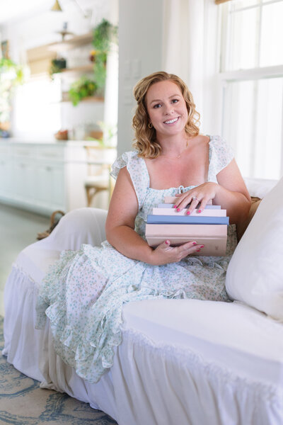 virginia beach photographer chelsey kraus holding stack of heirloom albums and smiling during branding photos