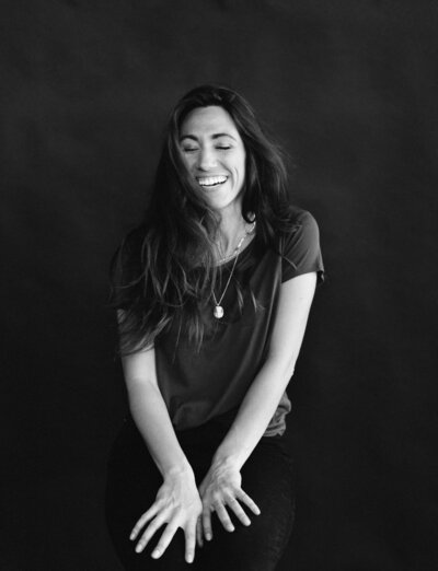 film brand headshot of woman laughing, hair movement, dark background, stationer branding photoshoot