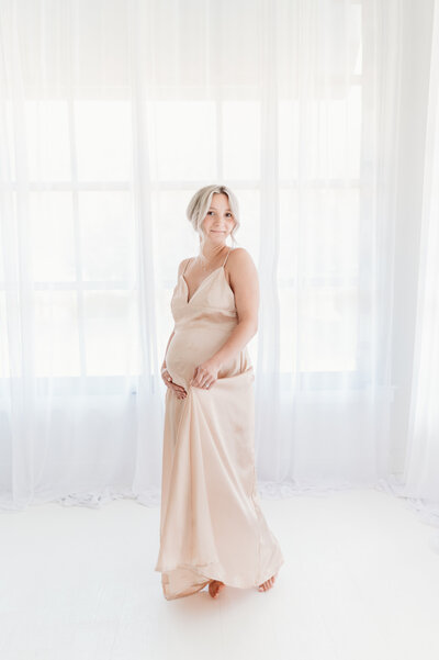 Pregnent mum to be in a light pink dress, holding her arm around her belly smiling during her maternity session in Atlanta