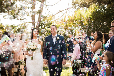 Bride and Groom walk down the aisle as guests blow bubbles