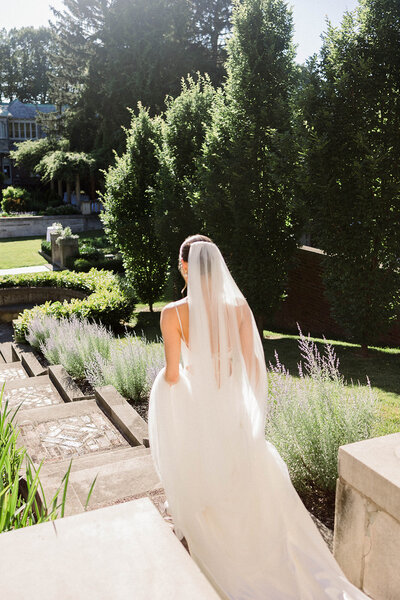 bride walking down estate stairs with sun glistening through her veil at the inn at irwin gardens