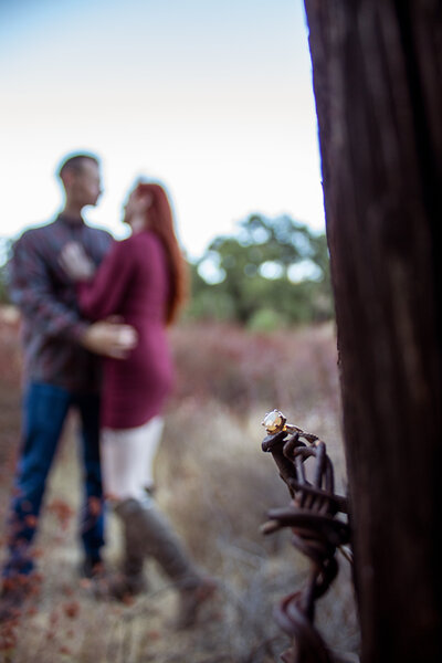 engagement ring with couple embracing in the background arizona field