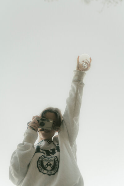 Woman taking film photo of camera from above while holding up a glass