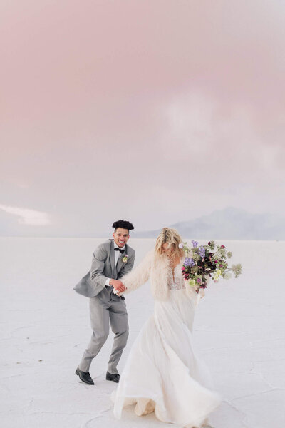 A groom playfully holds his brides hand at sunset at the Bonneville Salt flats on their wedding day. 