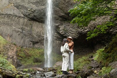 a lbgtq couple hug in front of a waterfall in the columbia river gorge in oregon