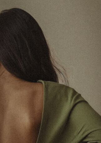 A serene woman with long hair, her back turned, wearing a soft green outfit, symbolizing peace and grounded energy.