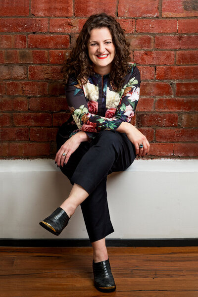 business woman seated with arms cross over legs in front of brick wall